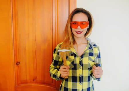 Attractive smiling builder woman with hammer and orange protective glassesの写真素材