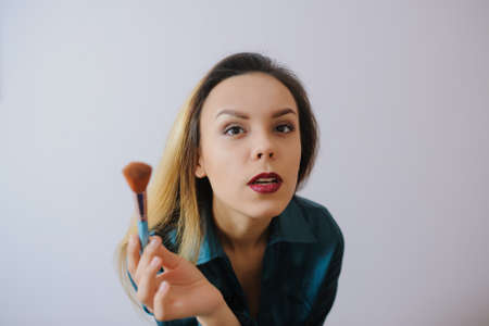 Portrait of sexy smiling happy caucasian young woman applying foundation blusher with makeup brushの写真素材