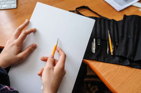 Top view of female hands with pencil on blank white paper sheet starting new pictureの写真素材