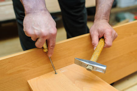 Worker repairing furniture with screwdriver and hammer. View of handsの写真素材