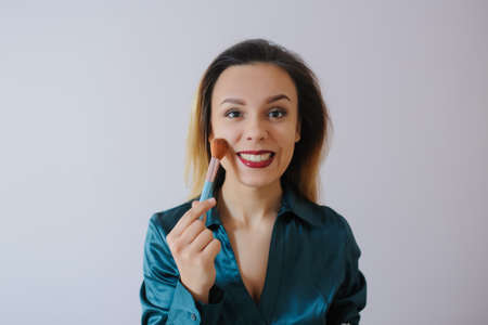 Portrait of sexy smiling happy caucasian young woman applying foundation blusher with makeup brushの写真素材