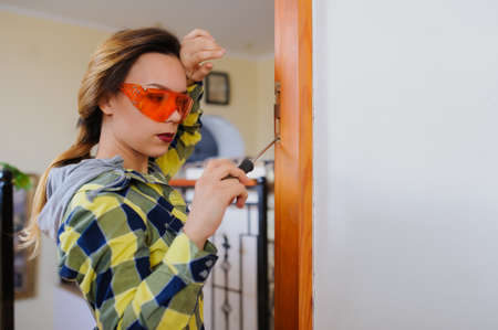 A young woman builder working using a screwdriver and fix the door. Orange protective glassesの写真素材
