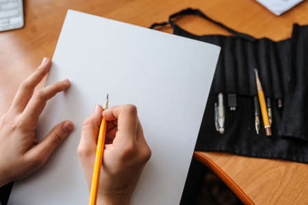 Top view of female hands with pencil on blank white paper sheet starting new pictureの写真素材