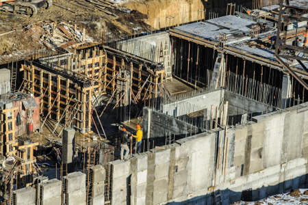 builders are working on a construction site, standing on a high wall and fixing metal fittingsの写真素材