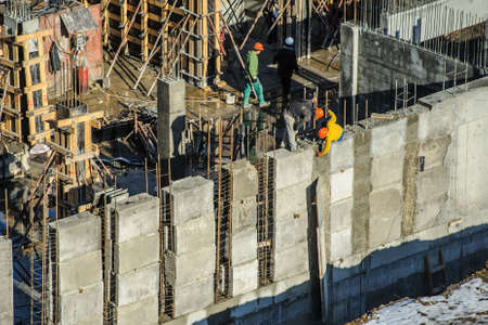 builders are working on a construction site, standing on a high wall and fixing metal fittingsの写真素材