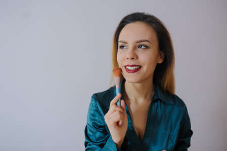 Portrait of sexy smiling happy caucasian young woman applying foundation blusher with makeup brushの写真素材