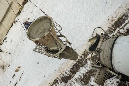 Concrete mixer truck pouring liquid concrete into the tower crane bucket at the construction site and construction engineer is monitors the process. Top viewの写真素材
