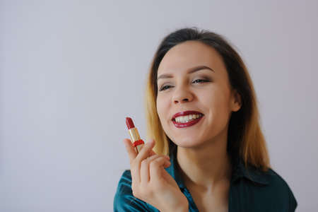 Portrait of sexy smiling happy caucasian young woman applying red lipstick on lips and looking at herself in the mirrorの写真素材