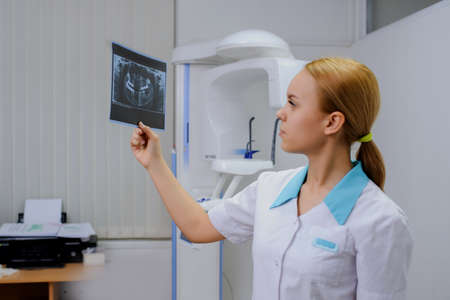 Young woman dentist analyzes a dental panoramic x-ray film in her clinic, after digital diagnostic examinationの写真素材