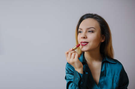Portrait of sexy smiling happy caucasian young woman applying red lipstick on lips and looking at herself in the mirrorの写真素材