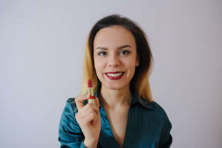 Portrait of sexy smiling happy caucasian young woman applying red lipstick on lips and looking at herself in the mirrorの写真素材