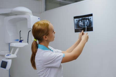 Young woman dentist analyzes a dental panoramic x-ray film in her clinic, after digital diagnostic examinationの写真素材