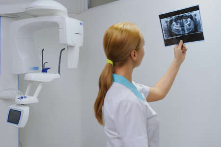 Young woman dentist analyzes a dental panoramic x-ray film in her clinic, after digital diagnostic examinationの写真素材