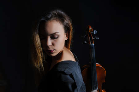 Beautiful young woman playing violin over black backgroundの写真素材