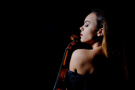 Beautiful young woman playing violin over black backgroundの写真素材