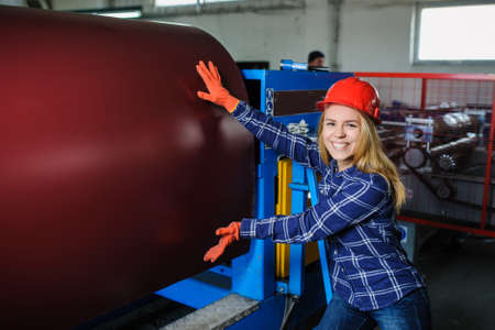 beautiful woman standing near metal coil at metal tile manufacturing factory and prepare it for profiling processの写真素材