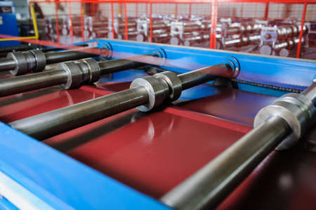 Metal tile manufacturing factory. Steel sheet metal roll profiling forming machine with rolls in working process.の写真素材