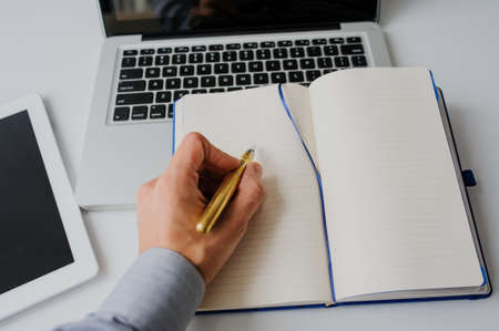 Top view of white studio workspace home office with laptop, blank notebook, computer, tablet and hand of businessmanの写真素材