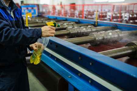 industrial worker spray on metal sheet profiling machine at manufacturing factoryの写真素材