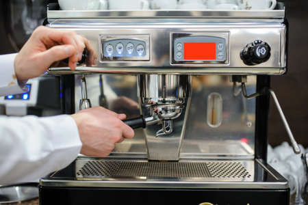 Closeup of a man barista brewing an espresso using a coffee machine in a coffee shopの写真素材