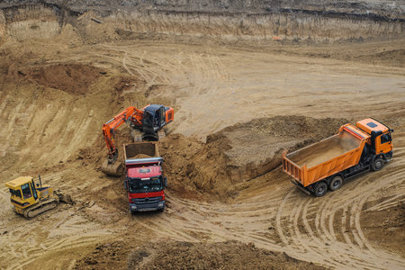 Industrial truck loader excavator moving earth and unloading into a dumper truck and bulldozer is...