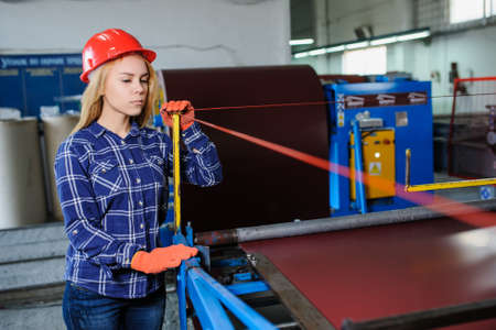 Portret of nice beautiful woman in red safety helmet at metal tile roof manufacturing factory examine the forming processの写真素材