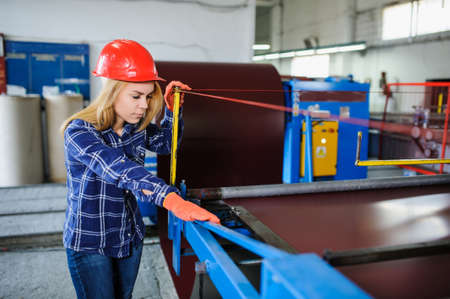 Portret of nice beautiful woman in red safety helmet at metal tile roof manufacturing factory examine the forming processの写真素材