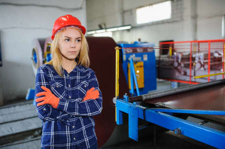 beautiful woman in red safety helmet work as industrial worker at metal sheet profiling mechine at manufacturing factoryの写真素材