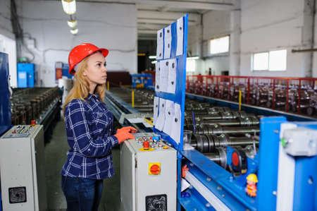beautiful woman in red safety helmet work as industrial worker at metal sheet profiling mechine at manufacturing factoryの写真素材