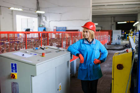 beautiful woman in red safety helmet work as industrial worker at metal sheet profiling mechine at manufacturing factoryの写真素材