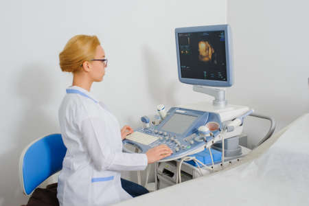 Young beautiful woman doctor working at ultrasound diagnostic machine usg and analyze the resultの写真素材