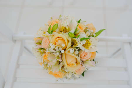 Beautiful fresh spring tender wedding bouquet of cream roses and eustoma flowers on wood white chairの写真素材