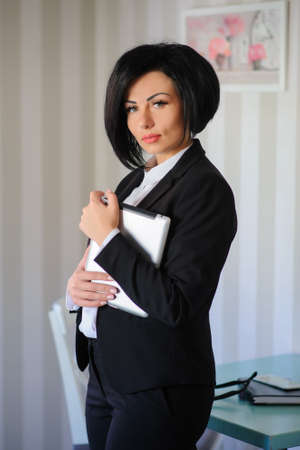 beautiful  business lady (woman/girl) dressed in black suit working on a tablet ( portable compute ) or is browsing internet in a vintage cafe/officeの写真素材