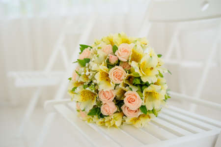 Beautiful fresh spring tender wedding bouquet of cream roses and eustoma flowers on wood white chairの写真素材