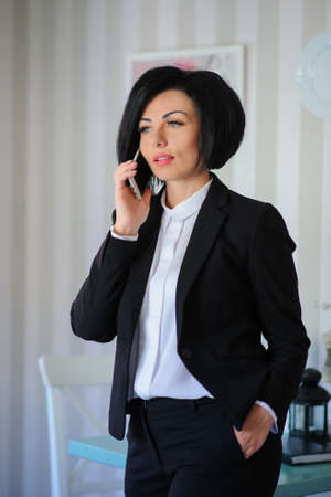 beautiful  business lady (woman/girl) dressed in black suit talking on the phone in a vintage cafe/officeの写真素材