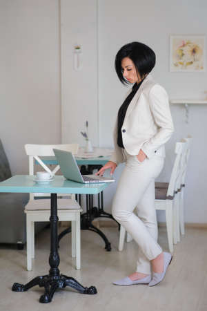 business lady dressed in white suit working on a laptop ( portable compute ) and have a cup of coffee on the table; beautiful woman is browsing internet; handsome girl with notebook;の写真素材
