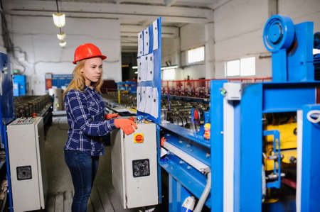 beautiful woman in red safety helmet work as industrial worker at metal sheet profiling mechine at manufacturing factoryの写真素材
