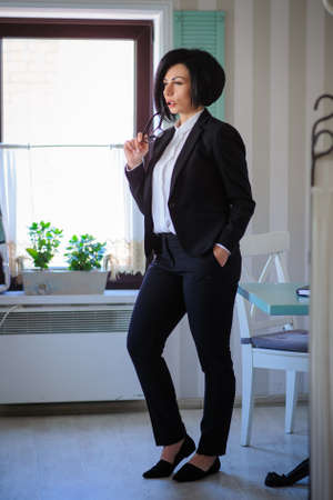 beautiful  business lady (woman/girl) dressed in black suit standing in a vintage cafe/officeの写真素材