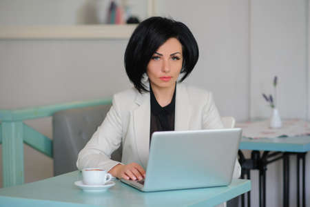 business lady dressed in white suit working on a laptop ( portable compute ) and have a cup of coffee on the table; beautiful woman is browsing internet; handsome girl with notebook;の写真素材