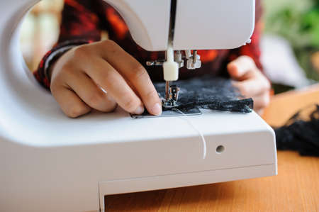 Young woman sewing  with sewing machine while sitting at her working place in fashion workshopの写真素材