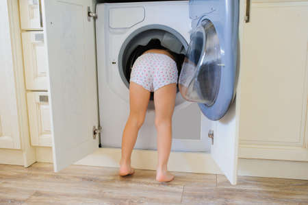 Little baby boy  putting his head into washing machineの写真素材
