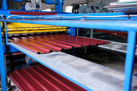 Metal tile manufacturing factory. Steel sheet metal roll profiling forming machine with rolls in working process.の写真素材