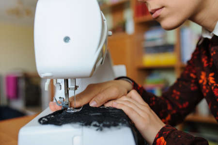 Young woman sewing  with sewing machine while sitting at her working place in fashion workshopの写真素材