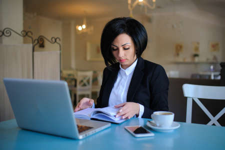 business lady dressed in black suit working on a laptop ( portable compute ) and have a cup of coffee on the table; beautiful woman is browsing internet; handsome girl with notebook;の写真素材