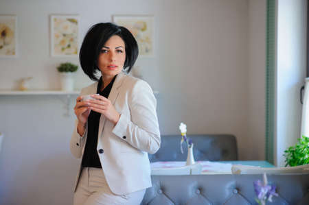 portrait of beautiful  business lady (woman/girl) dressed in white suit have a coffe breake in a vintage cafe/officeの写真素材