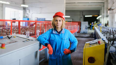 beautiful woman in red safety helmet work as industrial worker at metal sheet profiling mechine at manufacturing factoryの写真素材