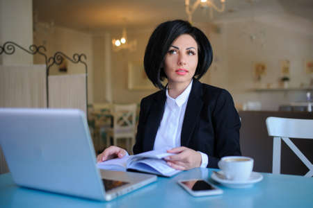 business lady dressed in black suit working on a laptop ( portable compute ) and have a cup of coffee on the table; beautiful woman is browsing internet; handsome girl with notebook;の写真素材