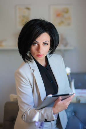 beautiful  business lady (woman/girl) dressed in white suit working on a tablet ( portable compute ) or is browsing internet in a vintage cafe/officeの写真素材