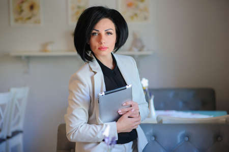 beautiful  business lady (woman/girl) dressed in white suit working on a tablet ( portable compute ) or is browsing internet in a vintage cafe/officeの写真素材