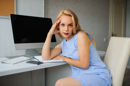 Serious young woman in blue dress working on a pc in her officeの写真素材